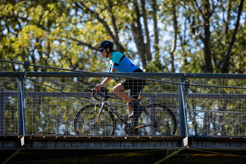women cycling across a bridge wearing the womens cycling jersey SYKL Pro 